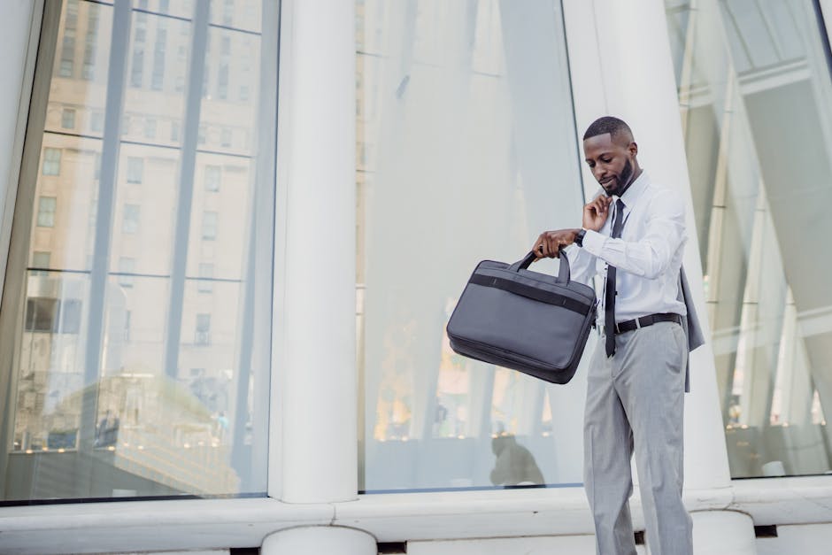 Professional man checking time with wristwatch while holding a laptop bag outside modern office